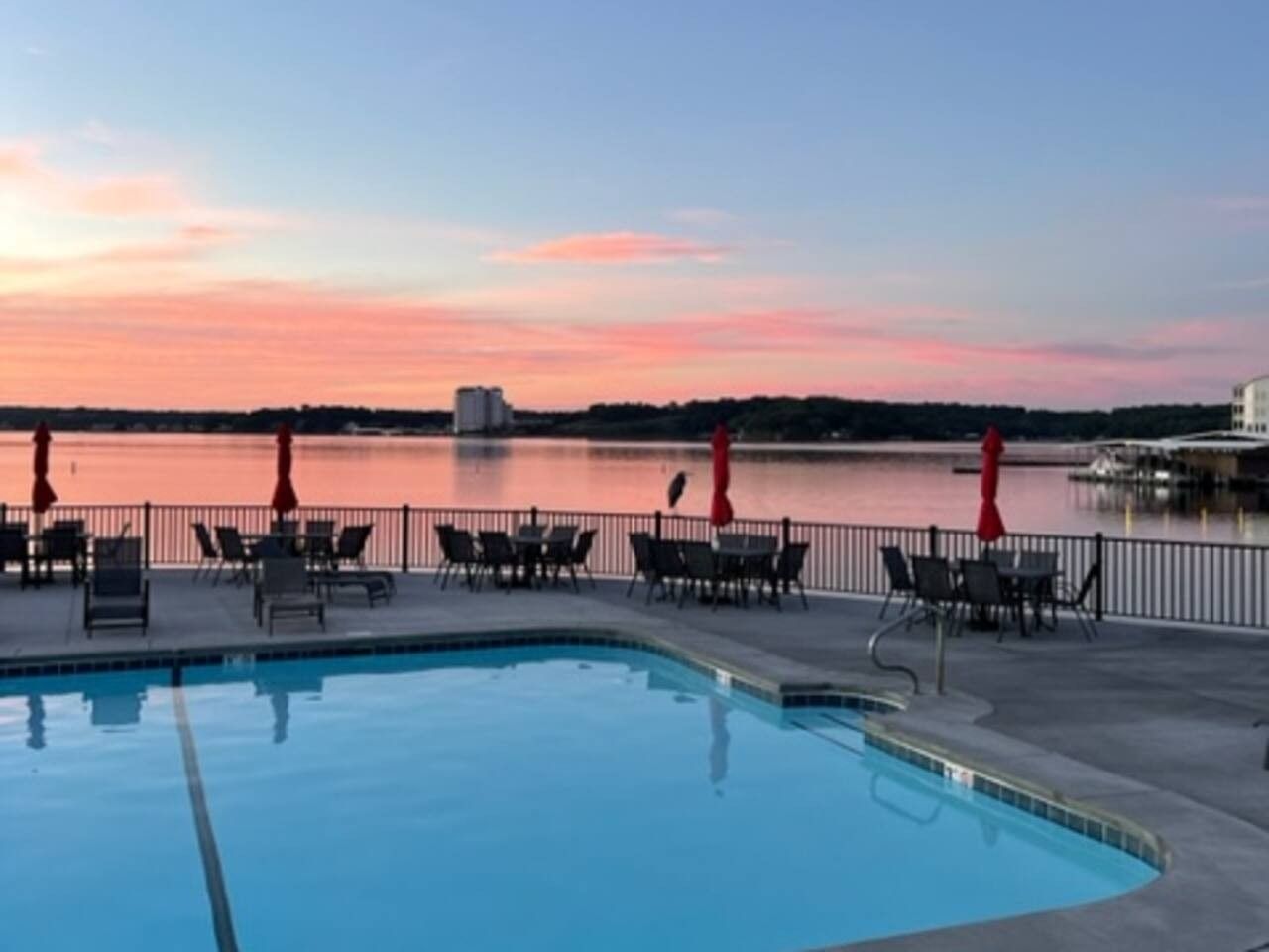 A swimming pool with lounge chairs and umbrellas, overlooking a body of water with a sunset sky.