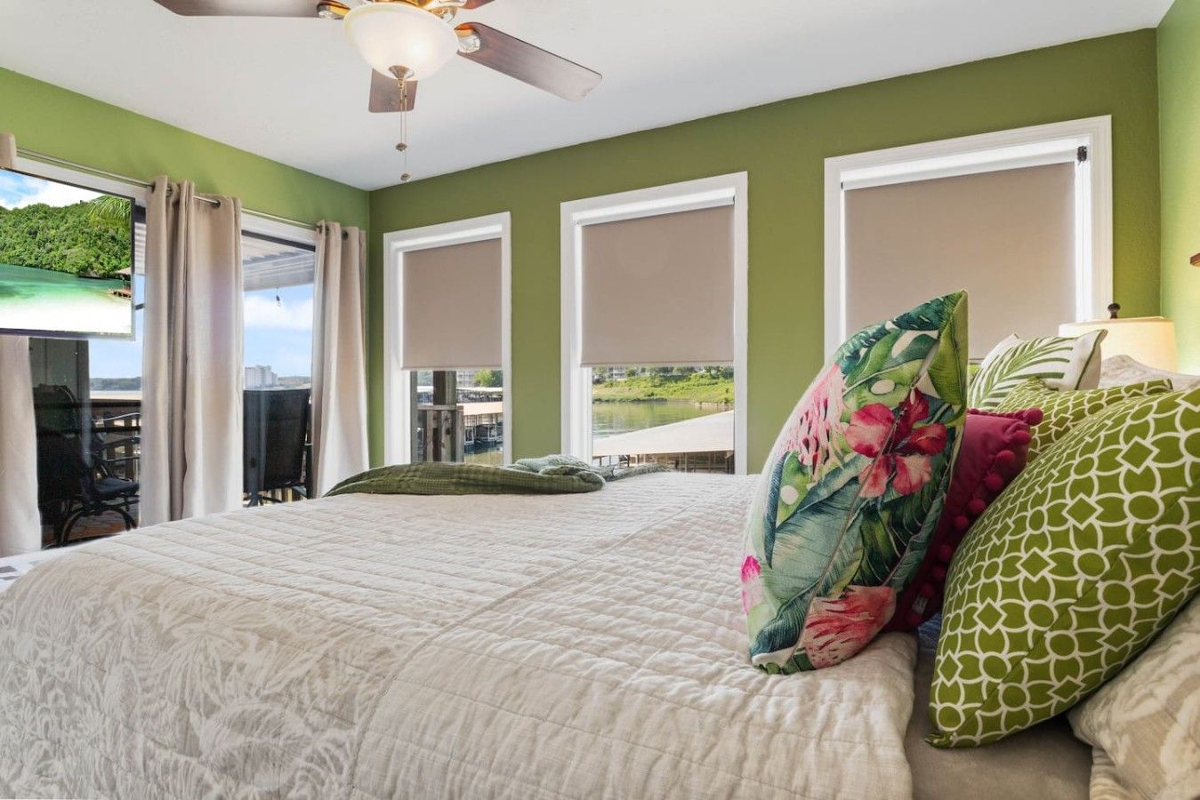A bedroom with a bed, a ceiling fan, and a view of a body of water through the window.
