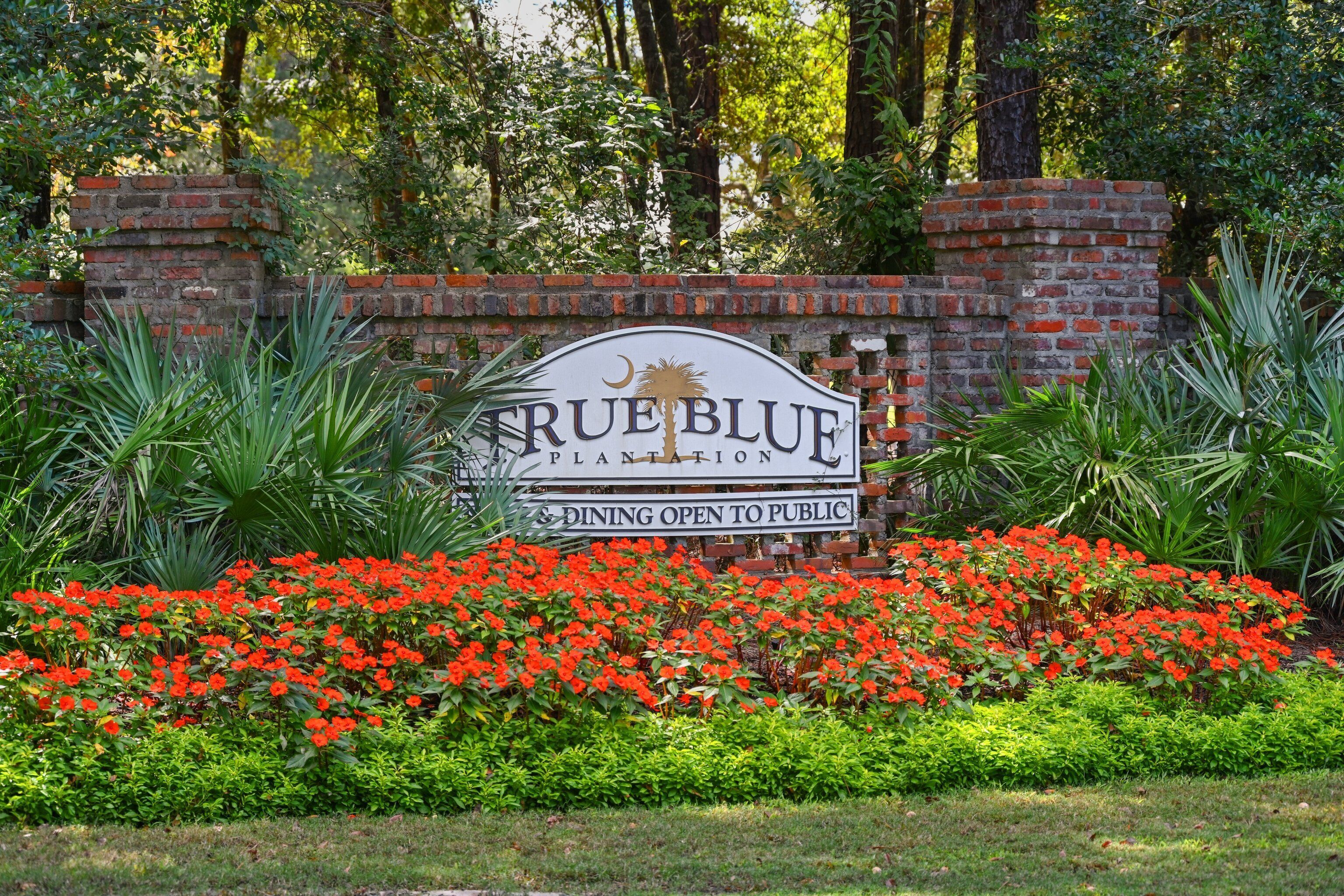 Letrero de True Blue Plantation, con un muro de ladrillo y abundante follaje.