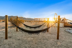 A hammock in a sandy area with wooden posts, a wooden structure in the background, and a sunset. - The White Owl House ☆pool ☆private ☆gorgeous views (Joshua Tree)