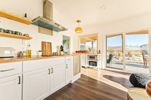 A kitchen with white cabinets, a wooden countertop, and a view of the outdoors through large windows. - The White Owl House ☆pool ☆private ☆gorgeous views (Joshua Tree)