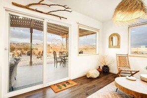 A room with a sliding glass door leading to an outdoor patio, a round wooden table, a wicker chair, and a hanging light fixture.