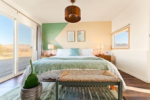 A bedroom with a bed, bedside tables, a hanging light fixture, a window, and a view of the outdoors. - The White Owl House ☆pool ☆private ☆gorgeous views (Joshua Tree)