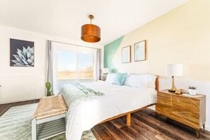 A bedroom with a large bed, bedside table, lamp, and a view of the outdoors.