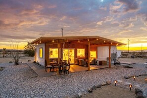 A single-story building with a covered patio area, outdoor seating, and a view of the desert landscape. - The White Owl House ☆pool ☆private ☆gorgeous views (Joshua Tree)