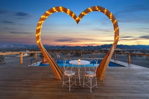 A wooden deck with a heart-shaped light installation, a pool, and a table with chairs. - The White Owl House ☆pool ☆private ☆gorgeous views (Joshua Tree)