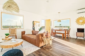 A spacious living area with a large window, a dining table, and a sofa. - The White Owl House ☆pool ☆private ☆gorgeous views (Joshua Tree)