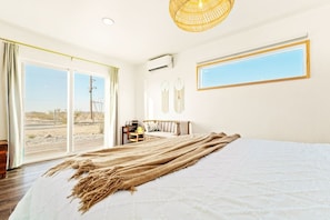 A bedroom with a large bed, a window with a view of the desert, and a ceiling fan. - The White Owl House ☆pool ☆private ☆gorgeous views (Joshua Tree)