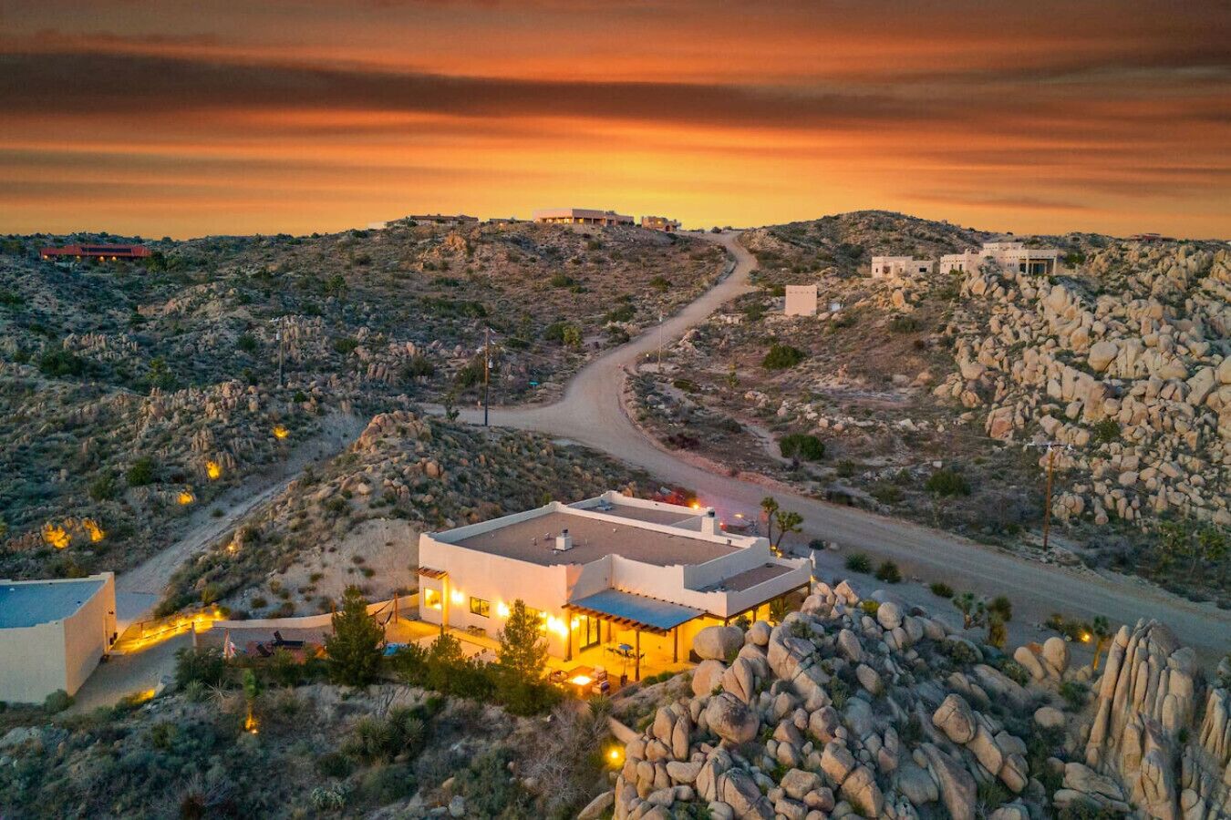 Une maison moderne avec une piscine, entourée d’un paysage rocheux et baignée par les couleurs d’un coucher de soleil.