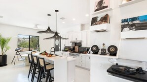 A modern kitchen with white cabinetry, a central island, pendant lighting, and a vinyl record collection on the counter.