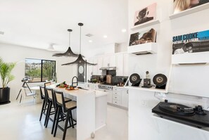 Une cuisine moderne avec des meubles blancs, un îlot central, des luminaires suspendus et une collection de disques vinyles exposée sur le comptoir.