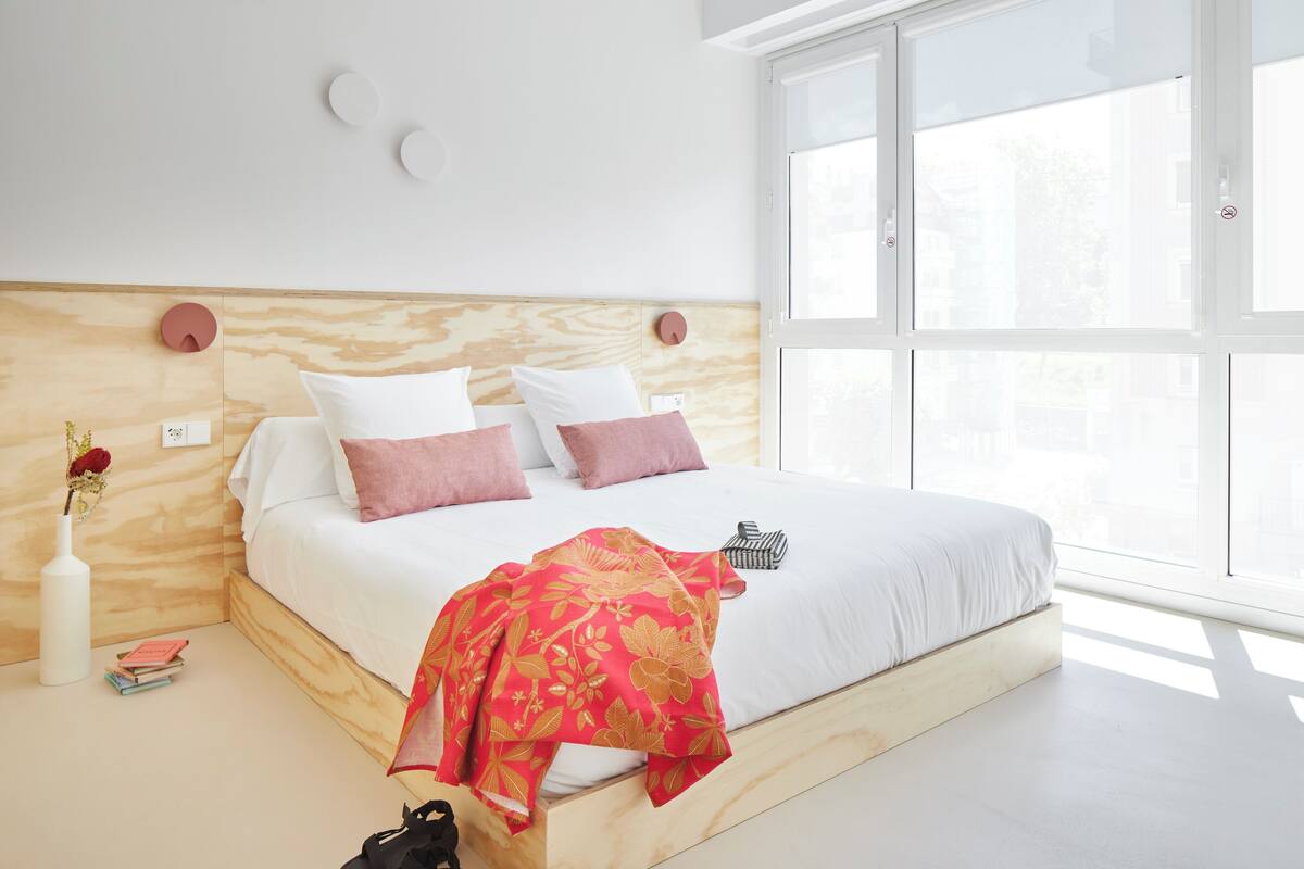 A modern bedroom with a wooden headboard, white bedding, and a large window providing natural light.