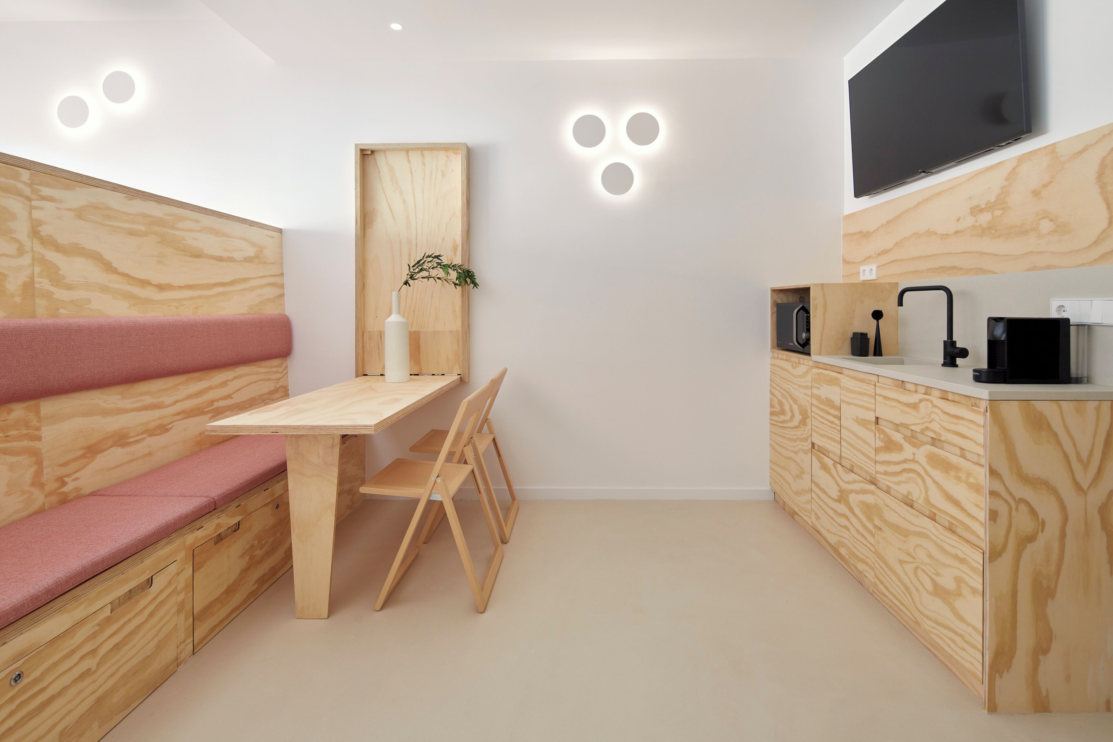 Een compacte keuken met een houten bank, een tafeltje en een aan de muur bevestigde televisie.