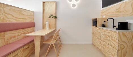 Een compacte keuken met een houten bank, een tafeltje en een aan de muur bevestigde televisie.