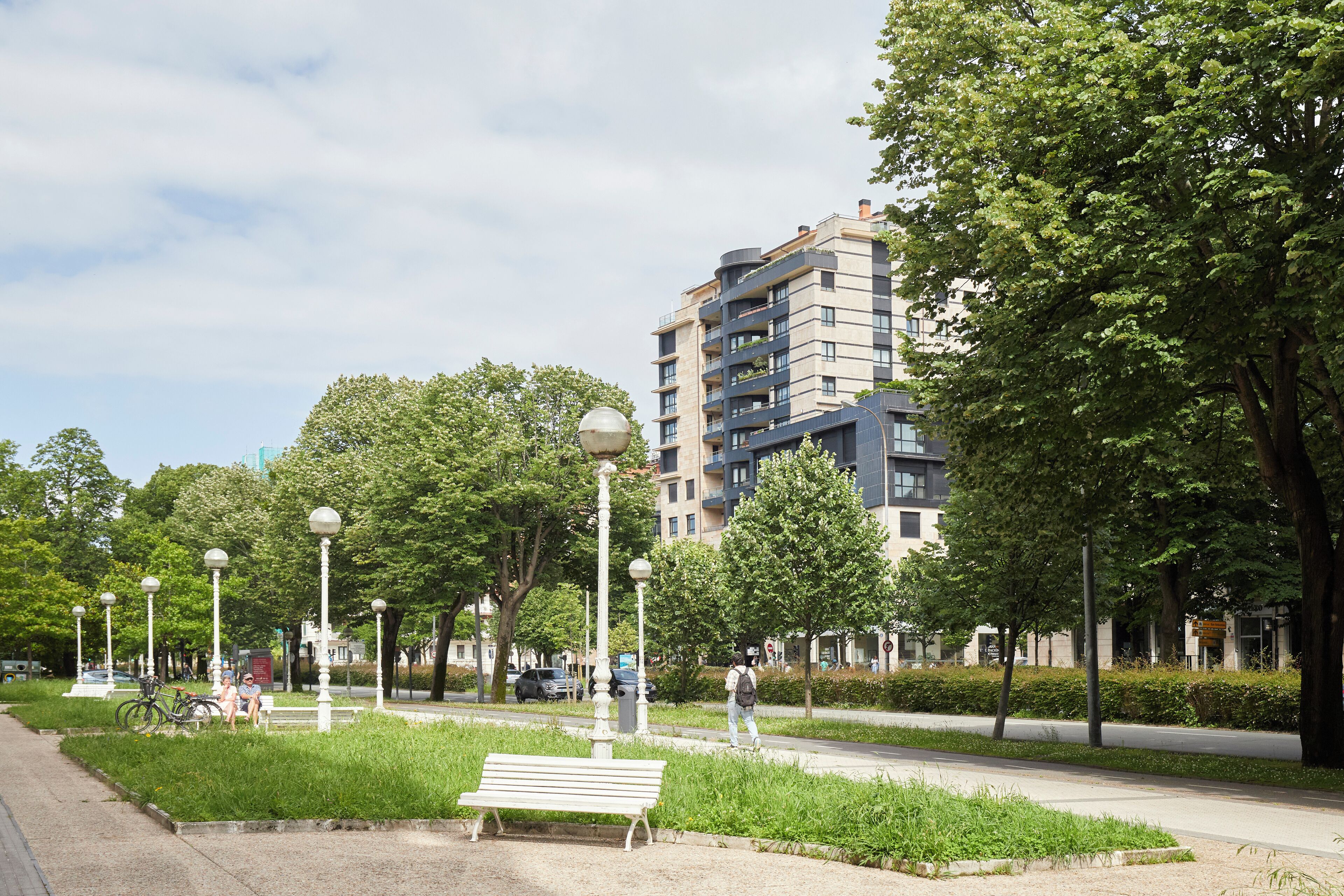 A park with a bench, trees, and a modern building in the background.