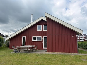 Ein rotes Gebäude mit Satteldach, Schornstein und einer kleinen Terrasse mit Holztisch und Stühlen.