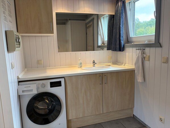 Cocina compacta con lavadora integrada, un lavamanos y un ventanal con cortinas.