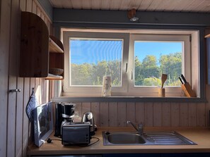 A kitchen with a window, wooden cabinets, a toaster, a coffee maker, and a sink.