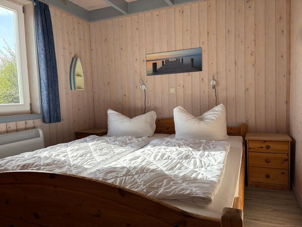 Un dormitorio con paneles de madera, una cama, almohadas, una mesita de noche y un cuadro en la pared.