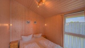 Una habitación de cabaña de madera con una cama, una mesita de noche y un ventanal.