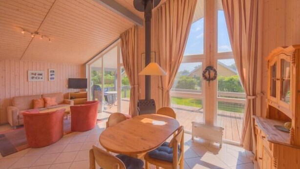 Una sala de estar acogedora con techo de madera, una mesa de comedor con sillas, un sofá y un televisor.