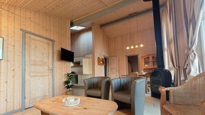 A cozy room with wooden walls, a wooden table, leather chairs, a television, and a fireplace.