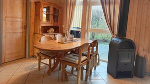A wooden interior with a round dining table, chairs, a cabinet, and a wood stove.