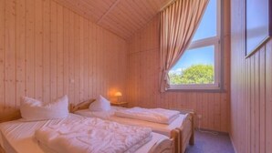 A wooden room with two beds, a window with curtains, and a nightstand with a lamp.