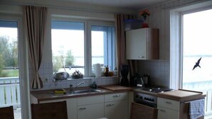 A compact kitchen with a dining area, large windows, and a view of the sea.