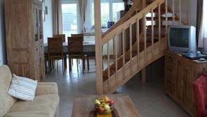 A living room with a wooden staircase, a dining area, and a television on a wooden cabinet.