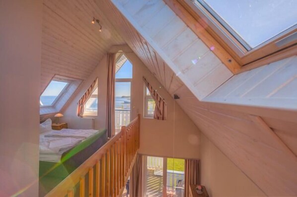 Ein Schlafzimmer im Loft-Stil mit Dachfenstern, einem Bett und Blick ins Freie.