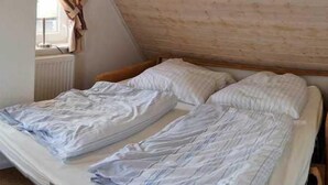 A small, single-room bedroom with a sloped ceiling and a radiator. There are two beds with white bedding and wooden headboards.