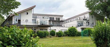 Un edificio de varios pisos con balcones, un patio césped y vegetación circundante.