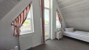 A bedroom with a sloped ceiling, a bed, a nightstand, a window with curtains, and a radiator.