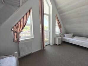 A bedroom with a sloped ceiling, a bed, a nightstand, a window with curtains, and a radiator. - Kapitänsdeck 475 - Großzügiges Ferienapartment auf 2 Ebenen mit Müritzblick (Rechlin-Nord)