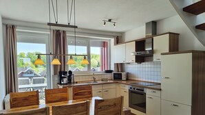 A modern kitchen with wooden chairs, a dining table, a window with curtains, and a view of houses.
