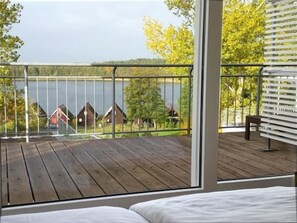 A balcony with a wooden deck overlooking a lake and houses. - Eisvogel Classic 301 - Großzügiges Lichtdurchflutetes Apartment auf 2 Ebenen (Mirow Ortsteil Granzow)