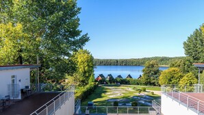 A terrace with a view of a lake, surrounded by trees and a small building with outdoor seating.