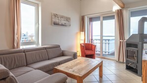 Ett vardagsrum med en soffa, ett soffbord i trä, en röd fåtölj, en öppen spis och stora fönster med gardiner.