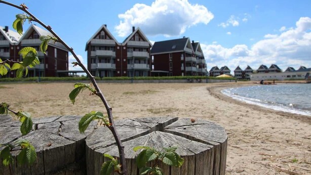 Ett hotell vid stranden med traditionell arkitektur, en sandstrand och en trästolpe i förgrunden.