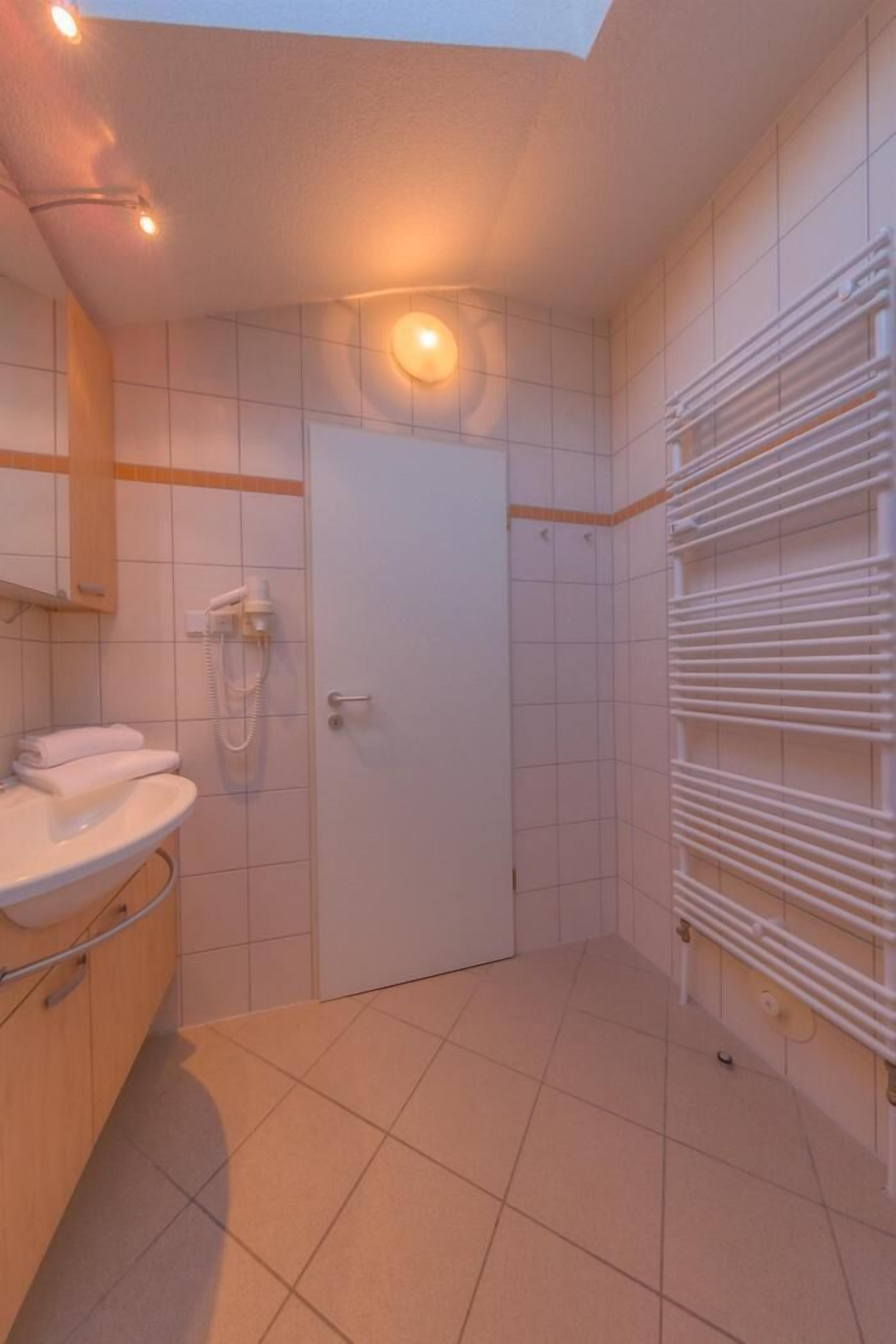 A modern bathroom with a white sink, a built-in toilet, a shower with a handheld showerhead, and a towel rack.