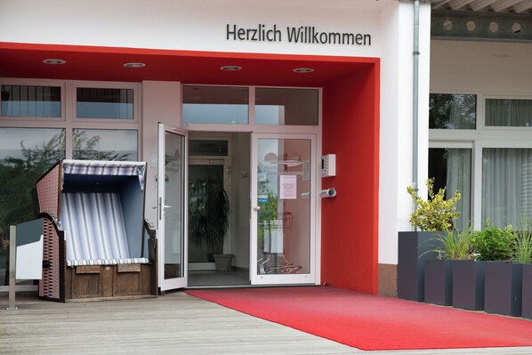 Ein Hotel Eingang mit einer roten Markise und einem Schild, auf dem 'Herzlich Willkommen' steht.
