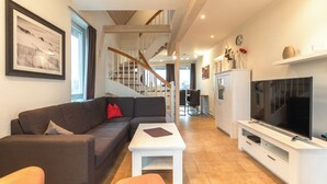 Una sala de estar moderna con un sofá, una mesa de centro y un televisor sobre un mueble blanco.