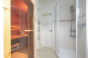 A bathroom with a glass-enclosed shower, a white door, and a tiled floor.