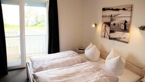 Une chambre d’hôtel avec deux lits, une porte-fenêtre coulissante donnant sur l’extérieur et une œuvre d’art accrochée au mur.