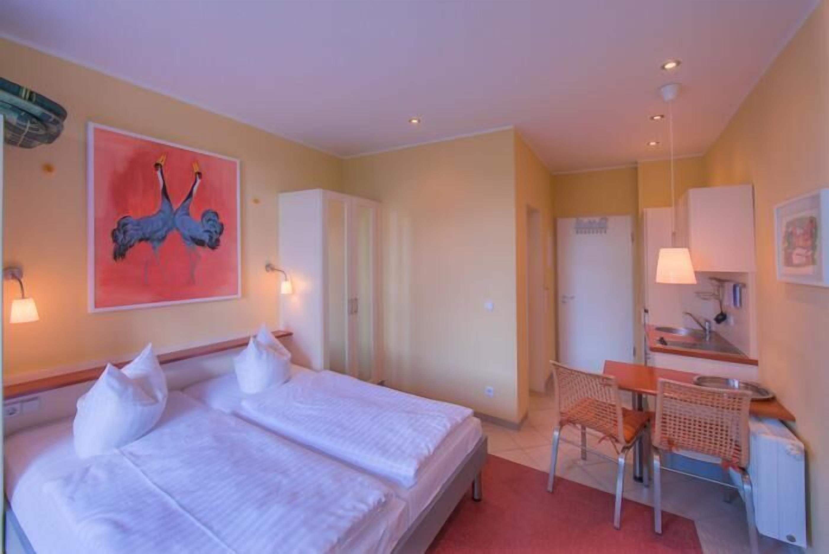 A hotel room with a double bed, a desk with a chair, a mirror, and a painting on the wall.