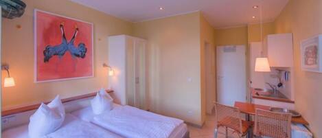 A hotel room with a double bed, a desk with a chair, a mirror, and a painting on the wall.