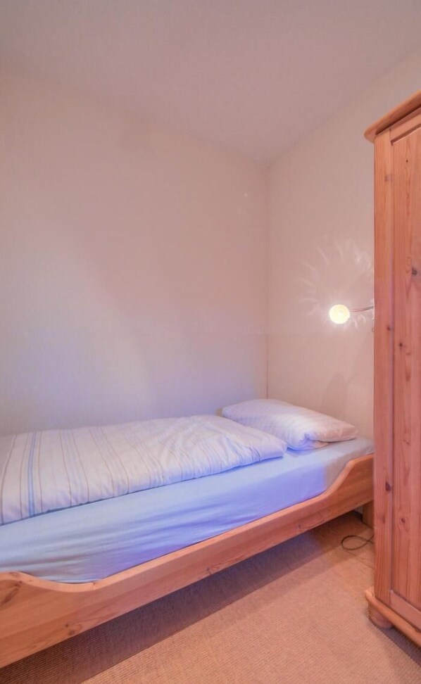A single bed with a wooden frame in a room with a light-colored wall and a wooden wardrobe.