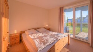 Et soveværelse med en træseng, et natbord, en lampe og en skydedør, der fører ud til en balkon.