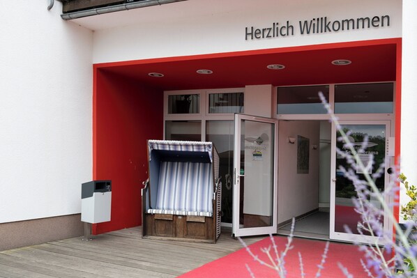 A hotel entrance with a red and white facade, a covered seating area, and a glass door leading inside.